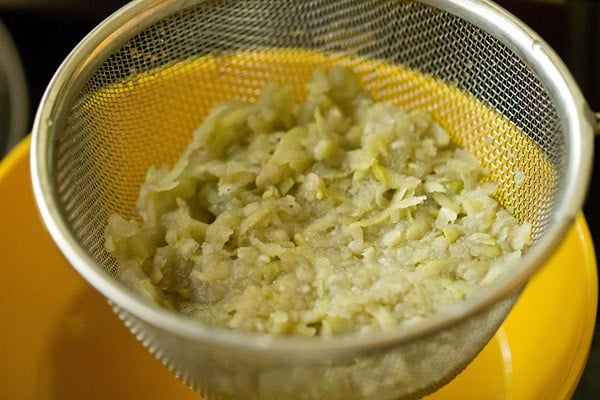 cooked lauki in a strainer above a yellow bowl to make lauki ka raita