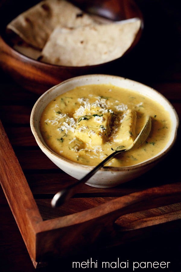 methi malai paneer garnished with grated paneer and served in a bowl with a side of roti.