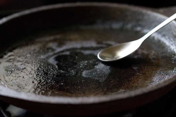 spreading the oil over the tawa using the back of a spoon