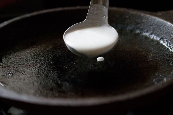 ladleful of dosa batter above the hot tawa