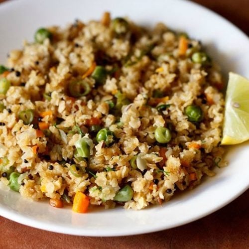 oats upma with lemon wedge on white plate on a brown board