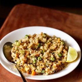 oats upma with lemon wedge and a spoon on white plate on a brown board