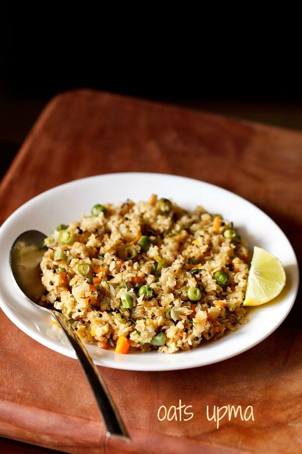 oats upma with lemon wedge and a spoon on white plate on a brown board