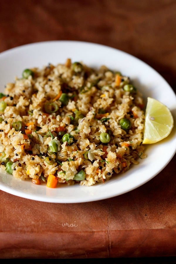 oats upma with lemon wedge on white plate on a brown board