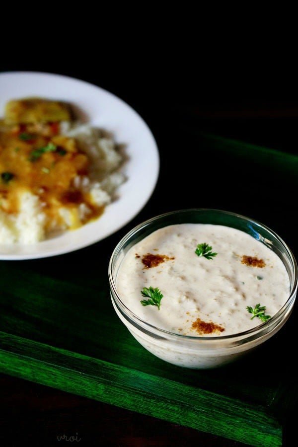 lauki raita in a glass bowl sprinkled with roasted cumin powder and coriander leaves on a dark green board