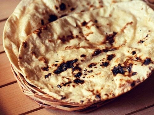 tandoori roti placed on top of a rattan roti box on a cream colored wooden board