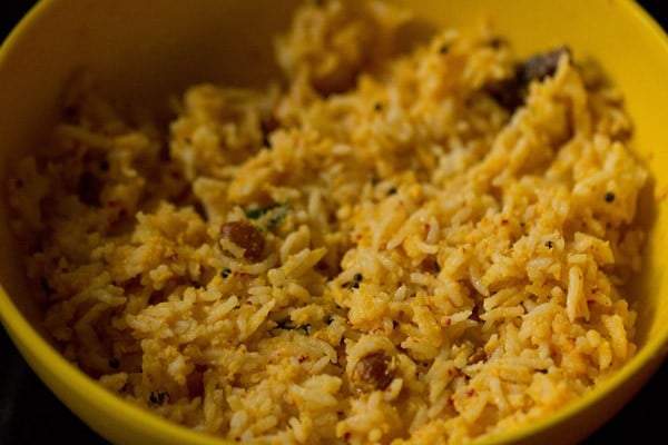 mixing raw-mango-coconut-spices masala with the cooked rice in the bowl. 