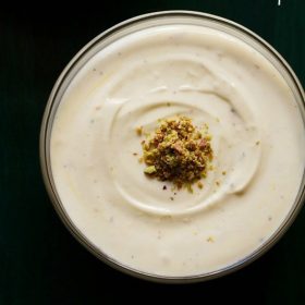 top shot of shrikhand with chopped pistachios on a dark green serving tray