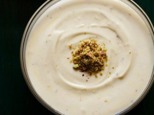 top shot of shrikhand with chopped pistachios on a dark green serving tray