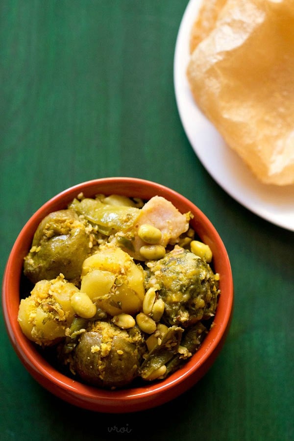 undhiyu served in a handi with a plate of pooris kept on the top right side. 