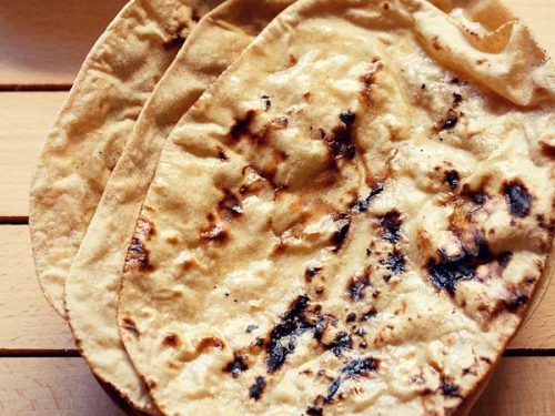 three tandoori roti placed on top of a rattan roti box on a cream colored wooden board