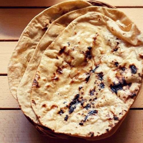 three tandoori roti placed on top of a rattan roti box on a cream colored wooden board