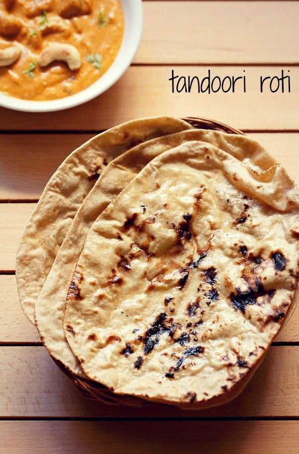 three tandoori roti placed on top of a rattan roti box on a cream colored wooden board