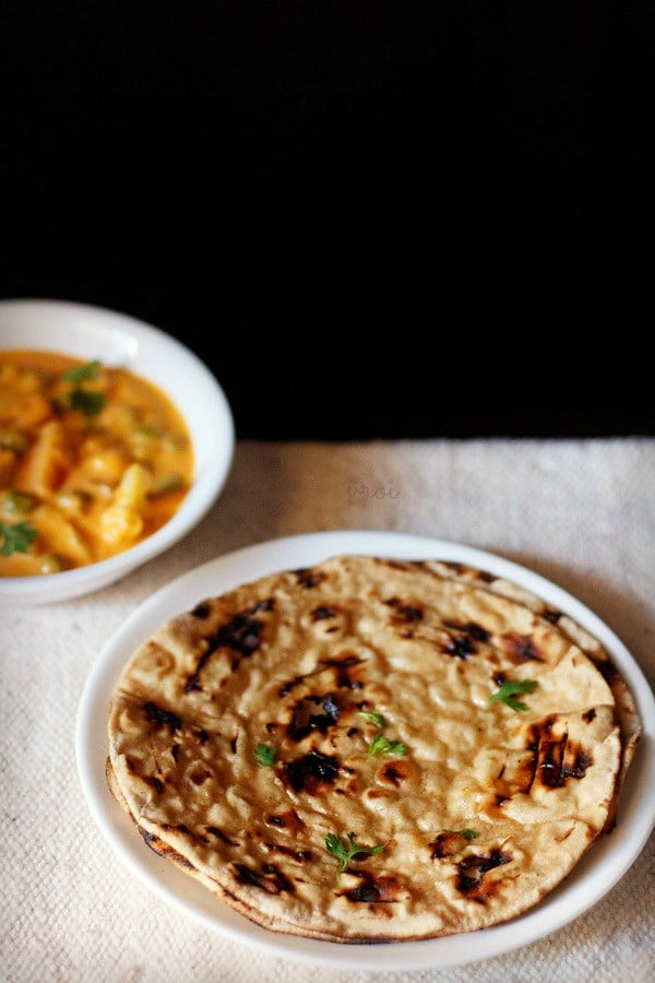 tandoori roti piled on a white dinner plate with a bowl of curry in the background.