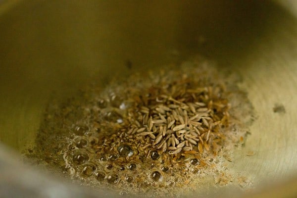 carom seeds and cumin seeds added to hot oil in a pressure cooker for undhiyu recipe.