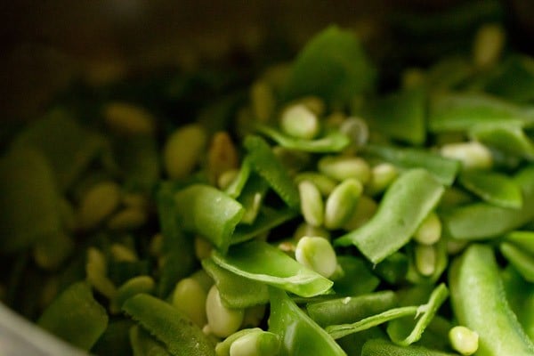 stringed and halved beans added to cooker for making undhiyu. 