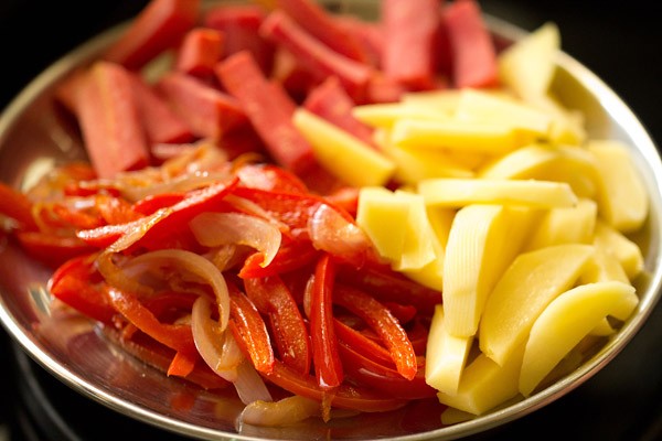 potatoes and carrots chopped in batons and sautéed onions, bell peppers in a steel plate