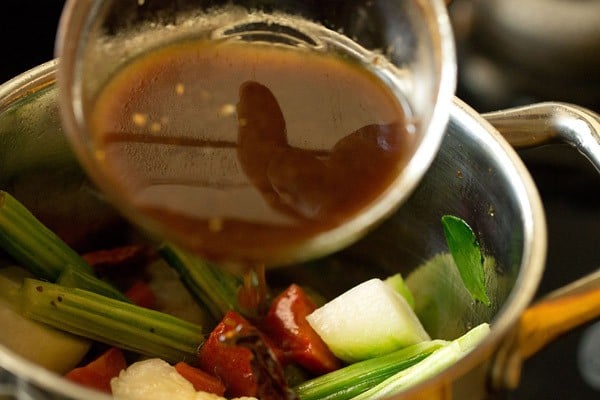 adding tamarind pulp and turmeric powder to vegetables in pan