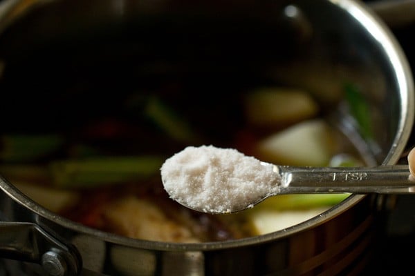 adding salt to the vegetables in pan