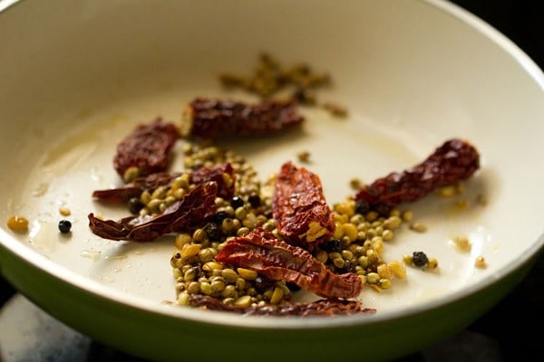 adding dried red chilies, coriander seeds, fenugreek seeds, Bengal gram and whole black pepper in hot sesame oil 