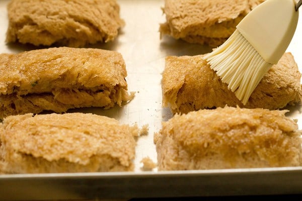 brushing prepared bread cheese rolls kept on a baking tray with oil. 