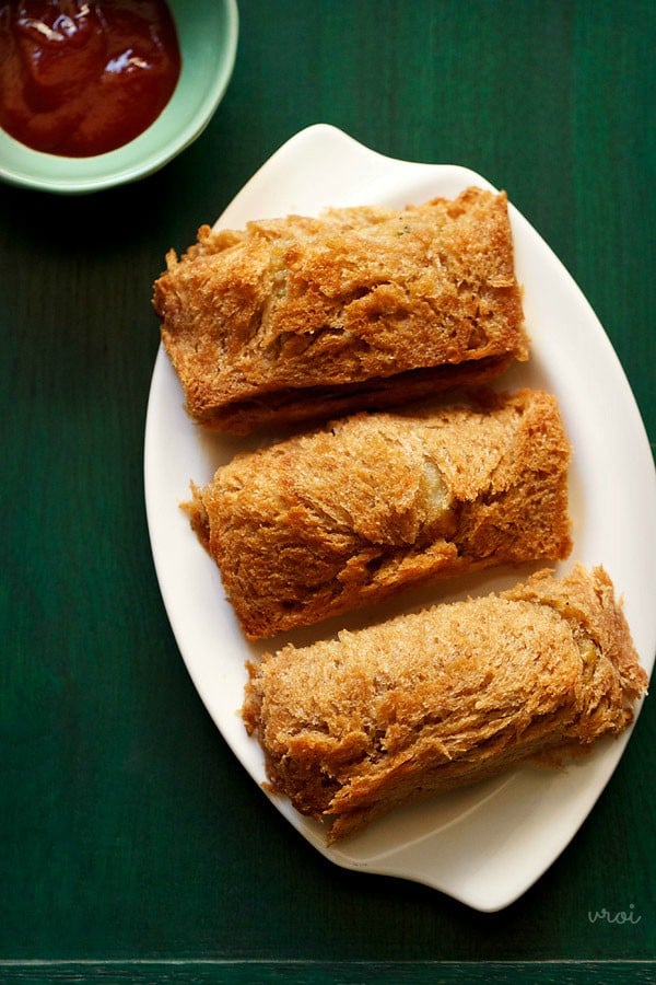 baked bread cheese roll served on a white plate with a small green color bowl of tomato ketchup kept on the top left side.  