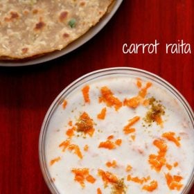 carrot raita served in a bowl with a plate of parathas kept on the top left side and text layover.