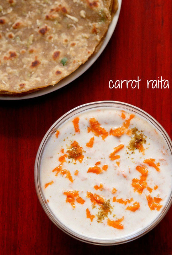 carrot raita served in a bowl with a plate of parathas kept on the top left side and text layover.