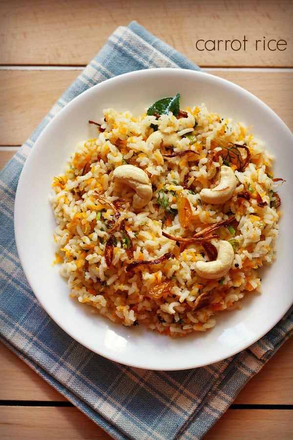 carrot rice garnished with cashews, fried onions and raisins served in a white plate on a checkered white and blue napkin