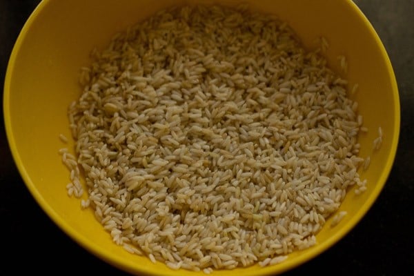 soaked and drained rice in a yellow bowl to make carrot rice recipe