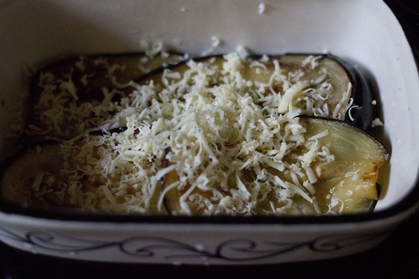 grated cheese on top of eggplant layer in a dish