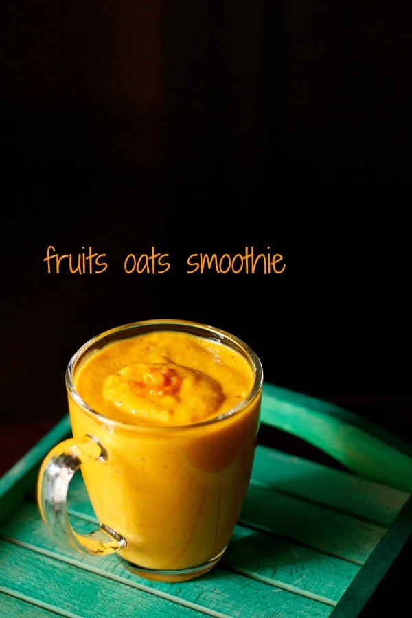 bright orange colored fruit and oatmeal smoothie in a glass mug on a green table.