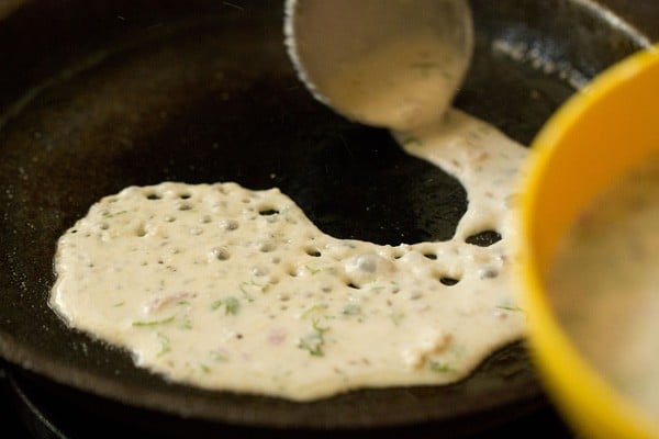 oats dosa batter added to pan using a ladle