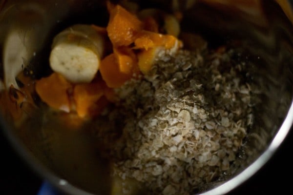 milk and oats added to blender jar with fruits for making smoothies.