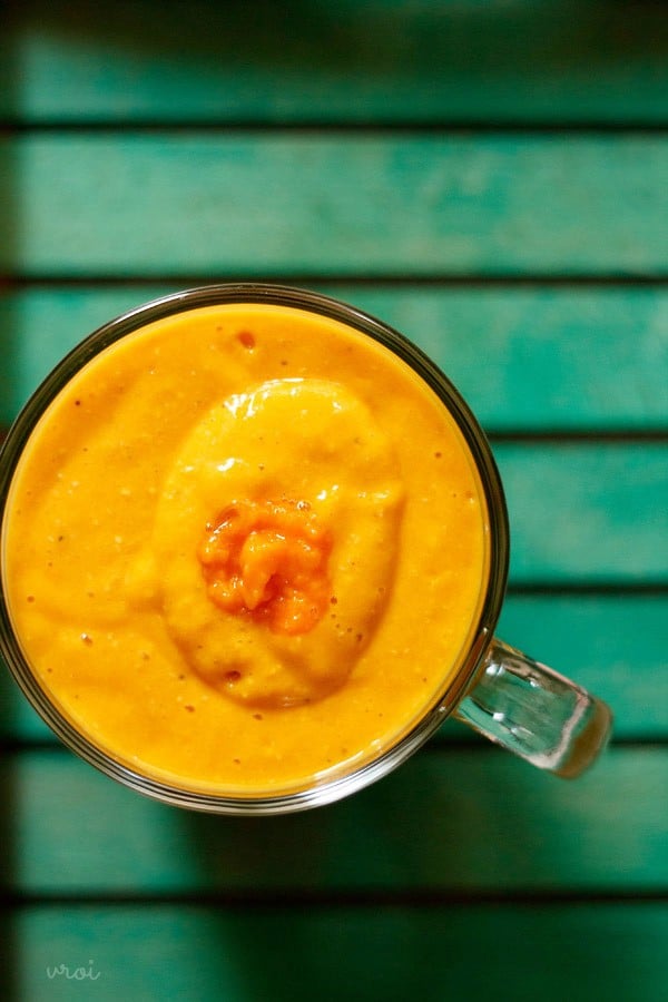 bright orange colored fruit and oatmeal smoothie in a glass mug on a green table. 