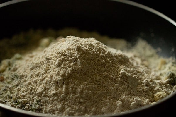 Closeup shot of oat flour added to sooji sautéing in black skillet.