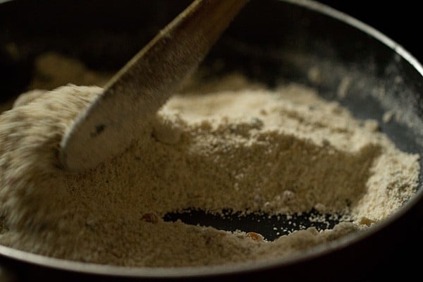 Wooden spoon stirring oat flour mixture in black skillet.