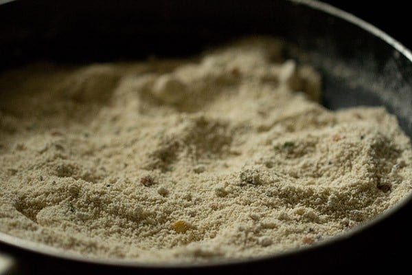 Closeup shot of oats flour roasting in black skillet for oats idli recipe.