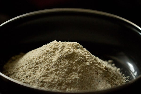 Oats idli flour mixture piled in black bowl.