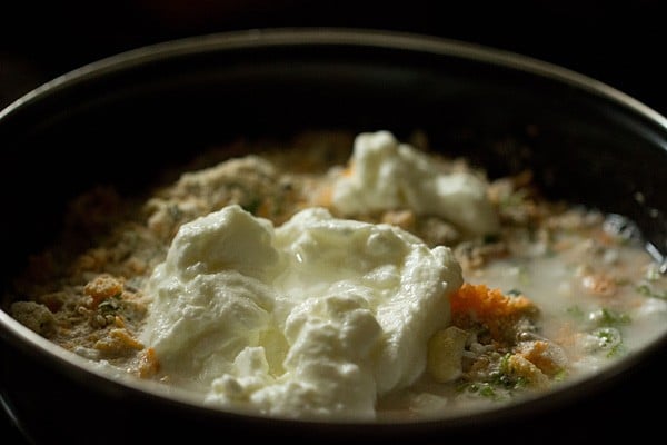 Curd and water added to oats batter in black bowl.