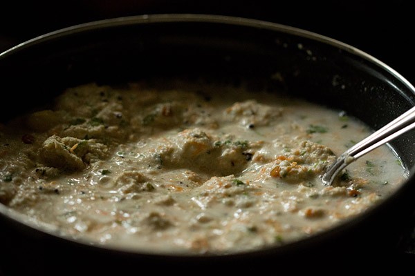 oats idli batter being stirred by silver spoon in black bowl.