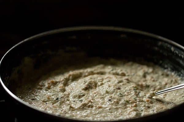 Silver spoon in oatmeal idli batter in black bowl.