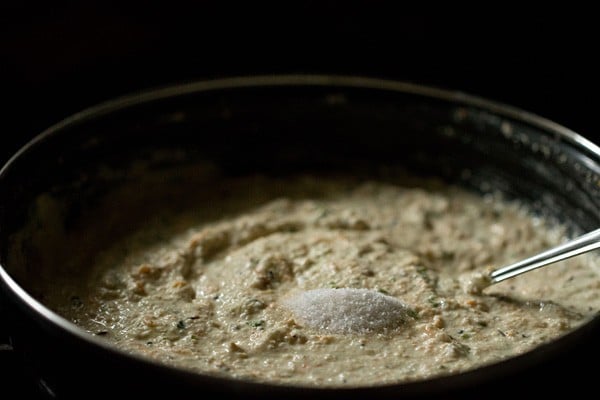 Salt added on top of oatmeal idli batter in black bowl.