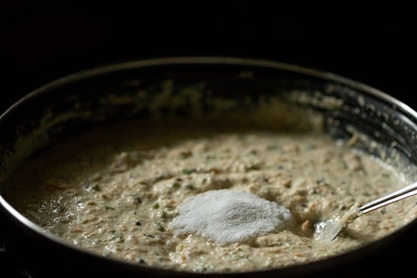 fruit salt added on top of oatmeal idli batter in black bowl.