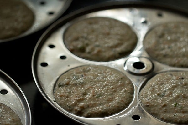 Idli mixture filling four greased moulds.