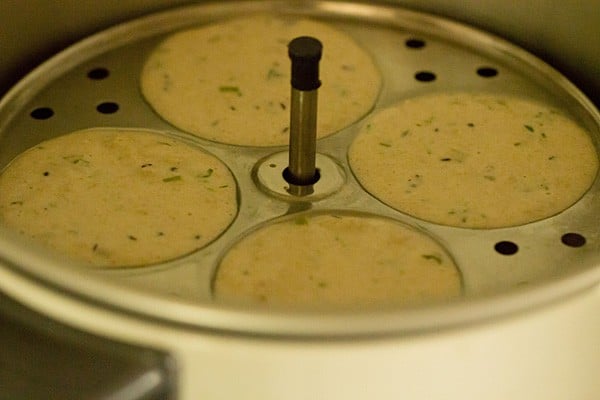 Filled idli mould cooking in electric cooker.