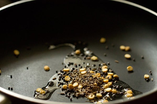 Seeds and lentils sautéing in oil in black skillet.