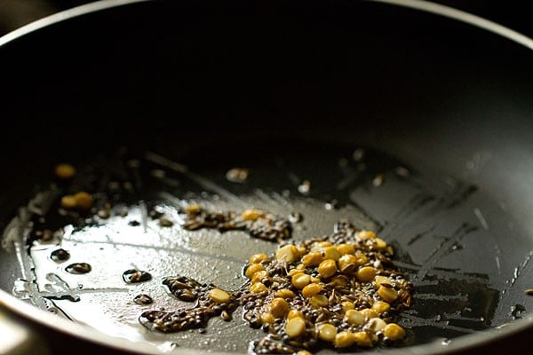 Seeds frying in oil in black skillet.