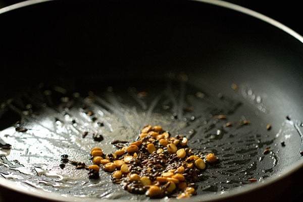 Seeds and lentils frying in oil in black skillet.