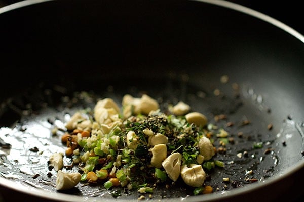 Ginger, nut, and seasoning mixture sautéing in black skillet.